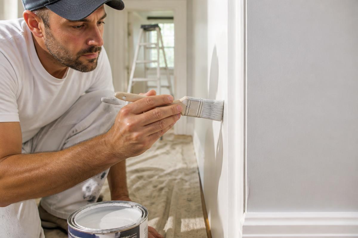 Orange Handyman carefully painting a clean wall edge